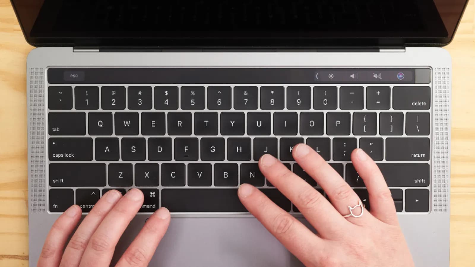 Hands typing on a laptop keyboard on a light wooden desk, seen from above