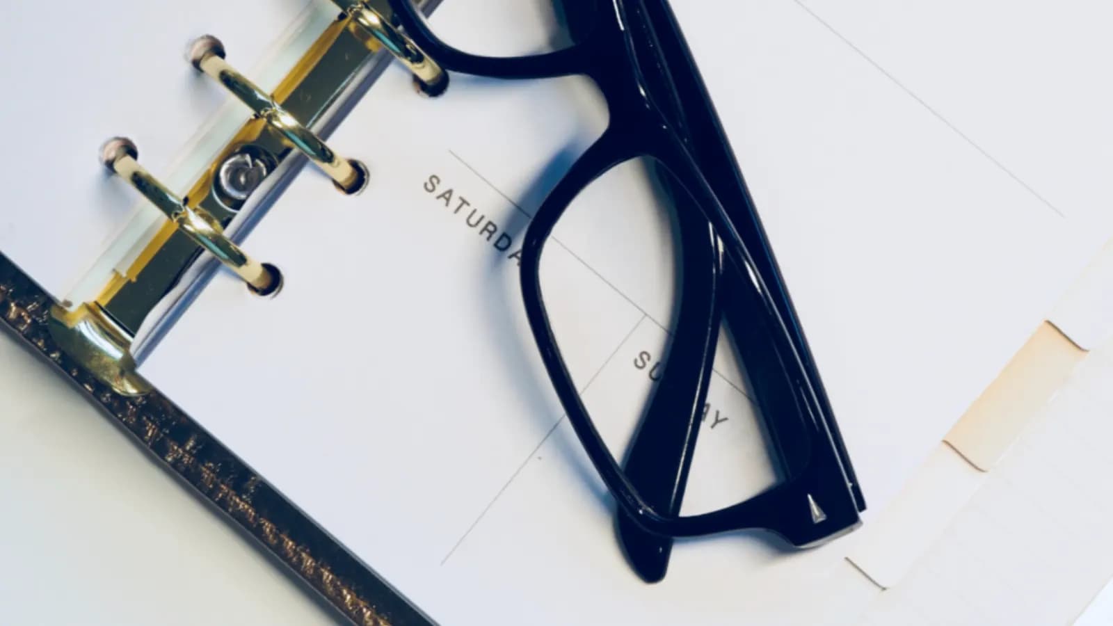 A pair of black glasses resting on an open weekly planner