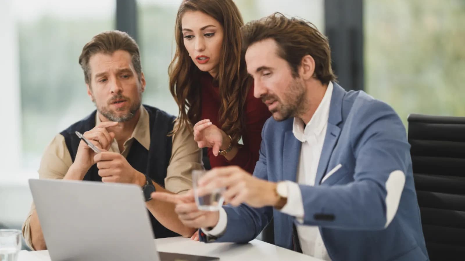 Three colleagues in an office looking at a laptop together while one points at the screen