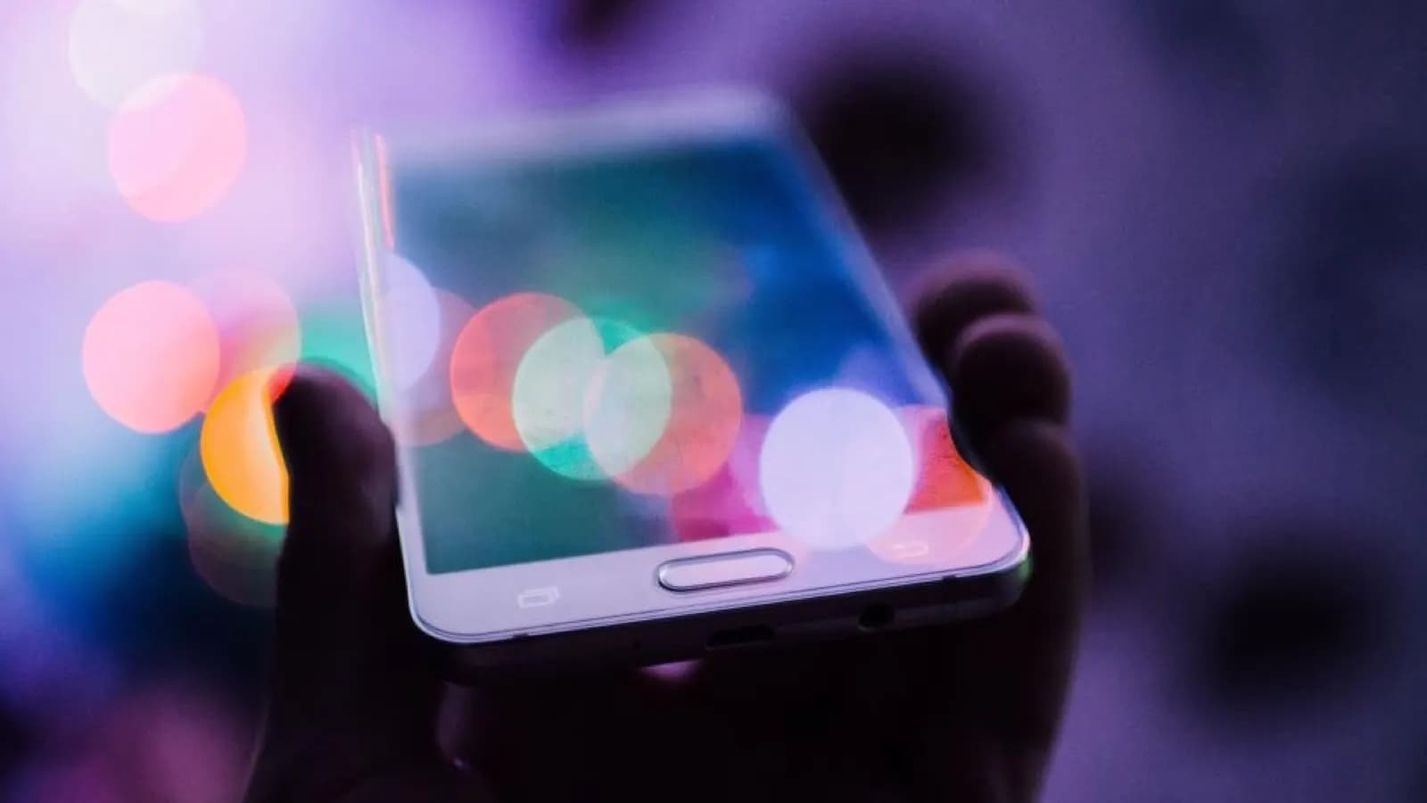 Hand holding a smartphone against blurred coloured lights, the moment before a call connects