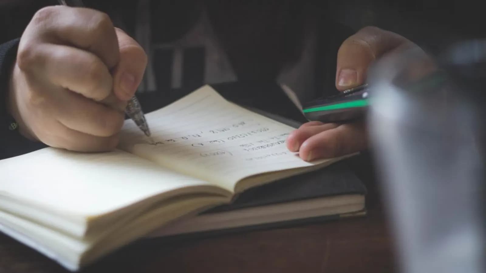 A person writing notes in an open notebook with a pen at a desk