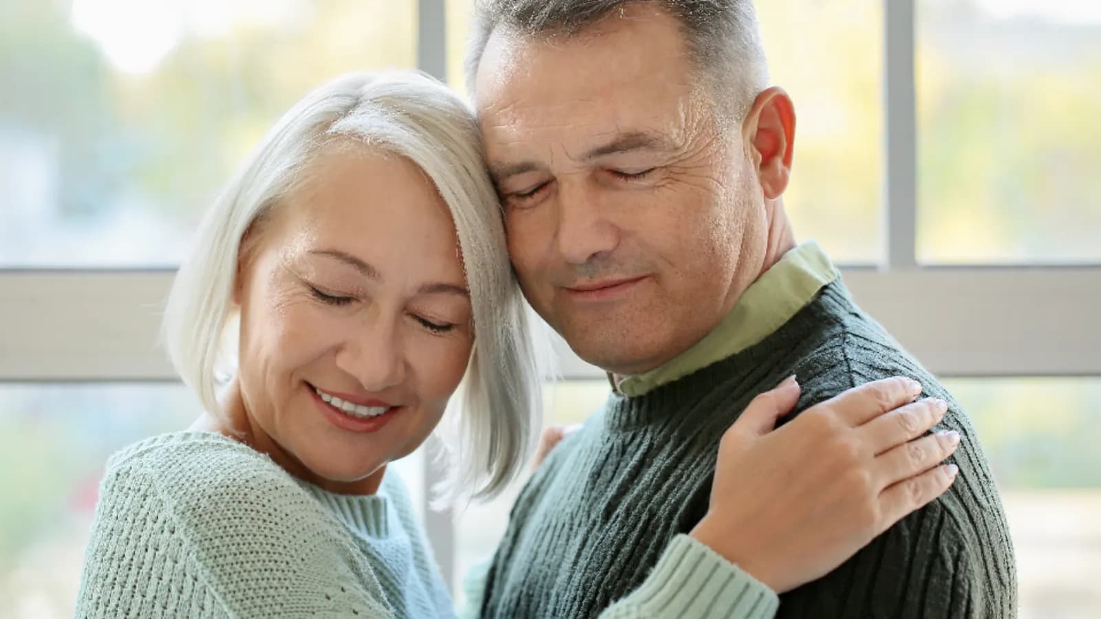 A smiling senior couple embracing at home by a bright window