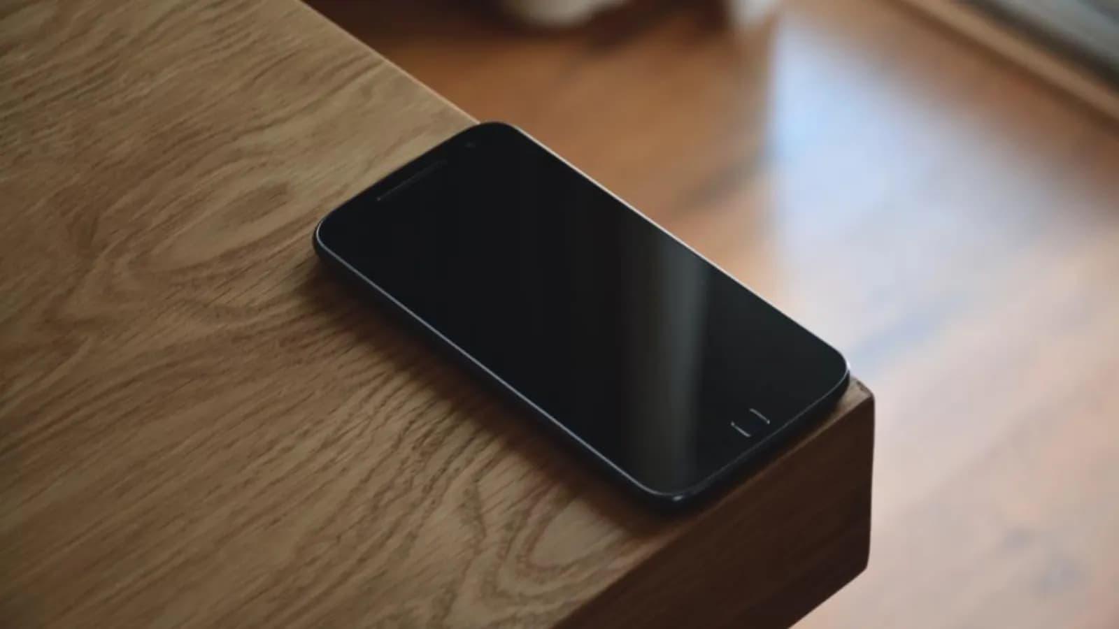 Smartphone lying face down on the corner of a wooden desk, waiting for an incoming call