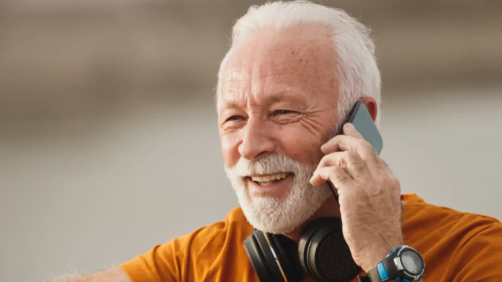 Smiling older man answering a call on his mobile phone outdoors, headphones around his neck