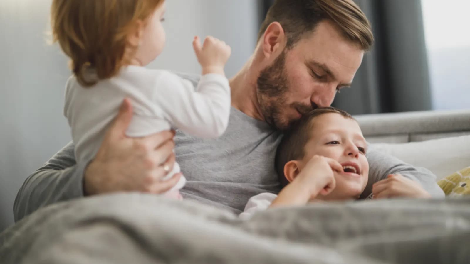 A father hugging his two young children on a sofa at home
