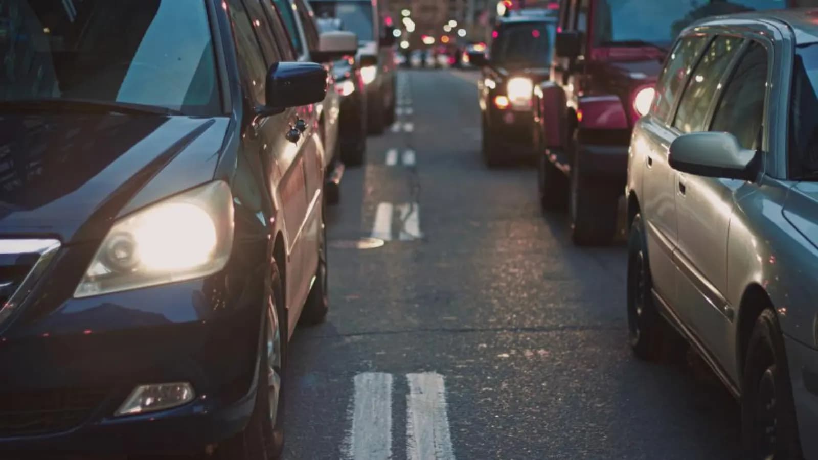 Cars queued in city traffic at dusk with their headlights on