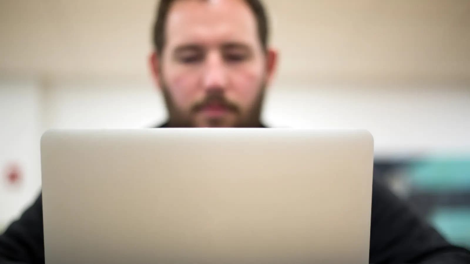 Support agent working on a laptop at a desk, face partly hidden behind the screen
